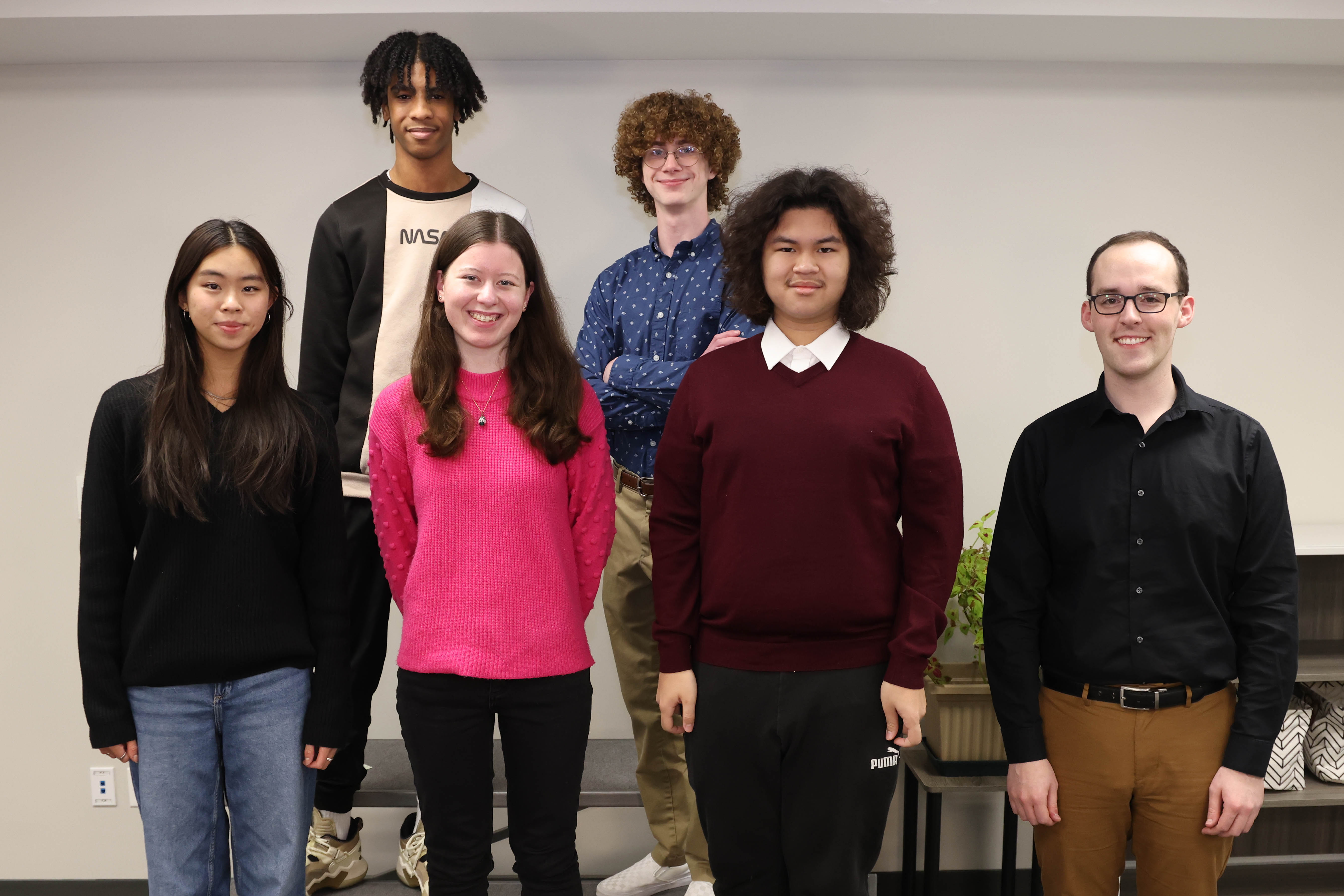 A group of students and one teacher are shown standing next to each other at a recognition program.